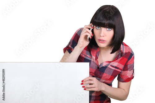 Photo: Brunette making telephone call by blank panel Brunette making telephone call by blank panel