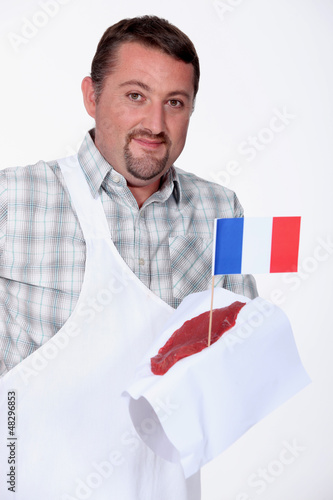 Photo: Butcher holding a piece of steak spiked with the French flag Butcher holding a piece of steak spiked with the French flag