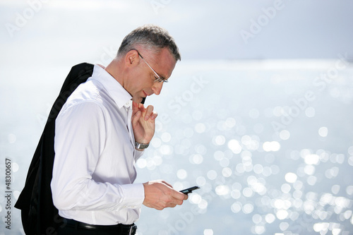 Photo: Businessman sending a text message by the seaside Businessman sending a text message by the seaside