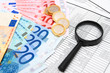 Magnifier, euro and coins on documents.