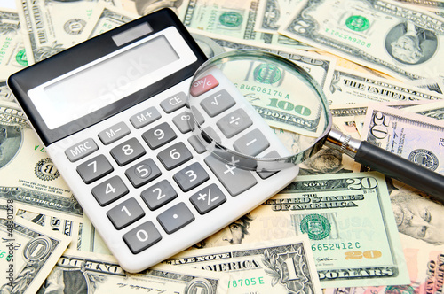 Photo: Calculator and magnifier on banknotes (dollars). Calculator and magnifier on banknotes (dollars).