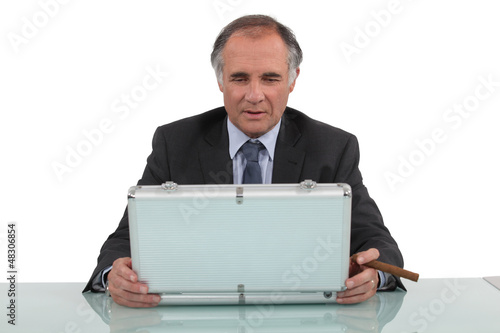 Photo: A businessman looking in a briefcase and smoking a cigar. A businessman looking in a briefcase and smoking a cigar.
