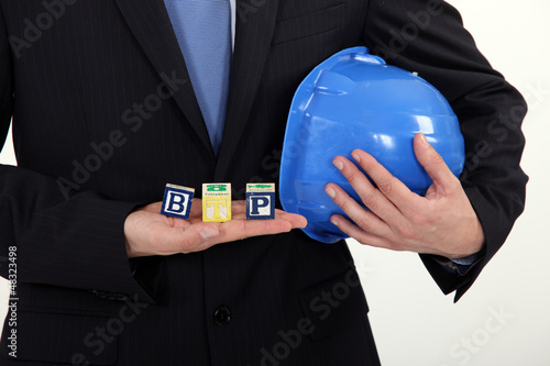 Photo: Businessman holding a hard hat and letter blocks Businessman holding a hard hat and letter blocks