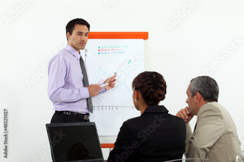 Photo: Man stood by flip-chart giving presentation to colleagues Man stood by flip-chart giving presentation to colleagues