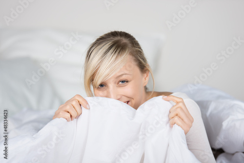Photo: lachende frau versteckt sich hinter bettdecke lachende frau versteckt sich hinter bettdecke