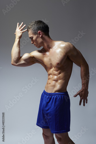 Photo: Muscular young man flexing arm muscles in sports outfit Muscular young man flexing arm muscles in sports outfit