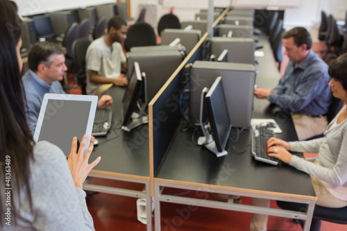 Photo: Woman holding a tablet pc while teaching her class Woman holding a tablet pc while teaching her class
