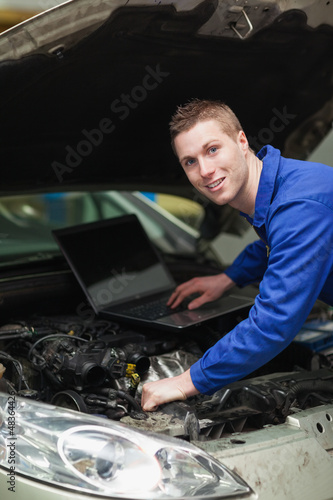 Photo: Car mechanic with laptop checking engine Car mechanic with laptop checking engine