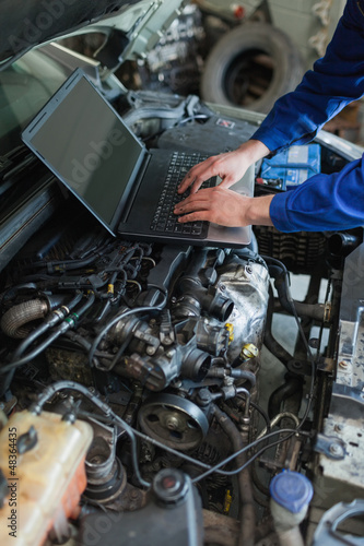 Photo: Mechanic hands using laptop on car engine Mechanic hands using laptop on car engine
