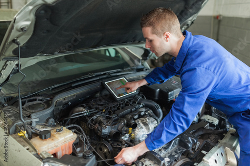 Photo: Mechanic with digital tablet repairing car engine Mechanic with digital tablet repairing car engine