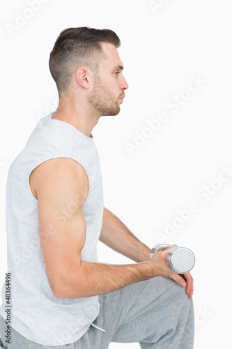 Photo: Side view of young man exercising with dumbbell Side view of young man exercising with dumbbell