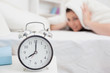 Woman covers ears with sheet as alarm clock rings