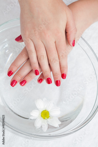 Photo: Red painted finger nails with flower in bowl Red painted finger nails with flower in bowl