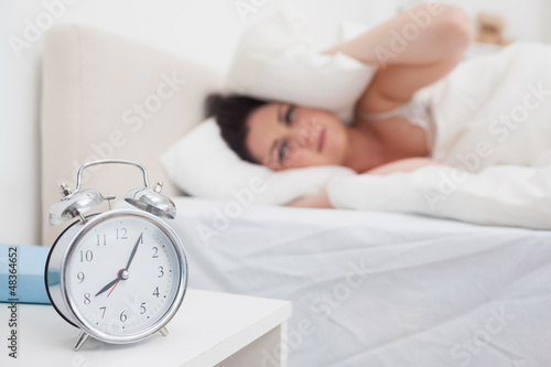 Photo: Woman covers ears with pillow as alarm clock rings in bedroom Woman covers ears with pillow as alarm clock rings in bedroom