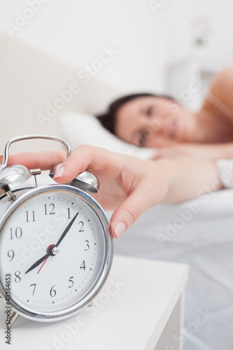 Photo: Woman in bed extending hand to alarm clock Woman in bed extending hand to alarm clock