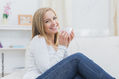 Photo: Smiling woman with coffee cup sitting on couch Smiling woman with coffee cup sitting on couch
