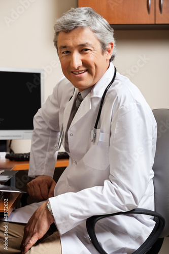 Photo: Male Doctor Sitting On Chair At Clinic Male Doctor Sitting On Chair At Clinic