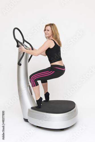 Photo: Eine junge sportliche Frau trainiert stehend auf Powerplate Eine junge sportliche Frau trainiert stehend auf Powerplate