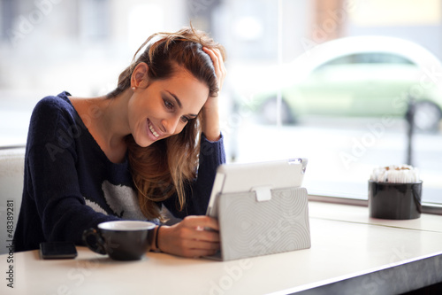 Photo: Candid image of a young woman using tablet computer in a coffee Candid image of a young woman using tablet computer in a coffee
