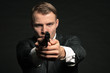 Man in suit shooting with gun. Studio shot against black.