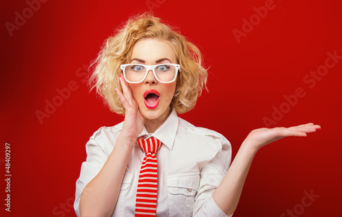 Photo: Surprised woman showing product, isolated on red background Surprised woman showing product, isolated on red background