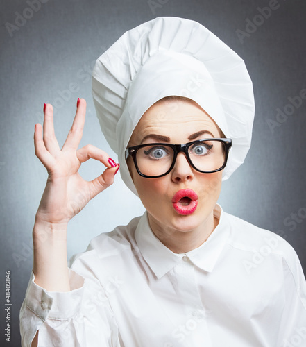 Photo: Young woman cook chef showing ok, isolated over gray wall Young woman cook chef showing ok, isolated over gray wall