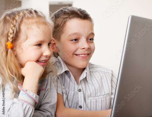 Photo: Happy kids playing laptop at home Happy kids playing laptop at home