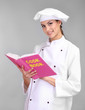 Portrait of young woman chef with cookbook on grey background
