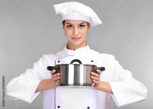 Photo: Portrait of young woman chef with pan on grey background Portrait of young woman chef with pan on grey background