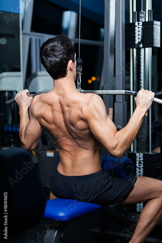 Photo: Athletic young man works out on simulator in fitness gym Athletic young man works out on simulator in fitness gym