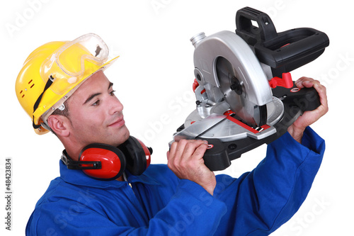 Photo: Construction worker examining his circular saw. Construction worker examining his circular saw.