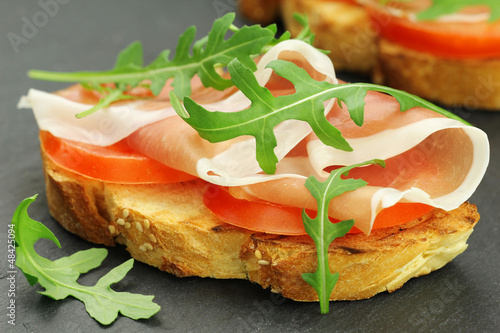 Photo: Italian bruschetta with prosciutto, rucola and tomatoes Italian bruschetta with prosciutto, rucola and tomatoes