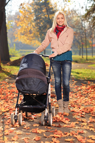 Photo: Mother taking a walk in park with her baby in a pushchair Mother taking a walk in park with her baby in a pushchair