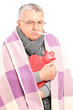 Sick senior with thermometer in his mouth, covered with blanket
