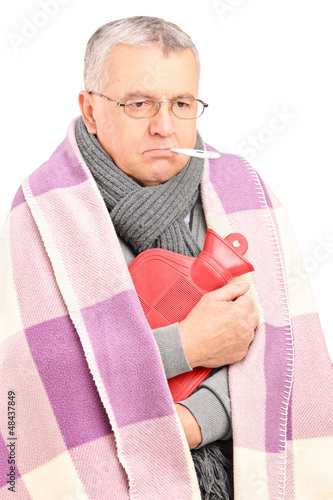 Photo: Sick senior with thermometer in his mouth, covered with blanket Sick senior with thermometer in his mouth, covered with blanket