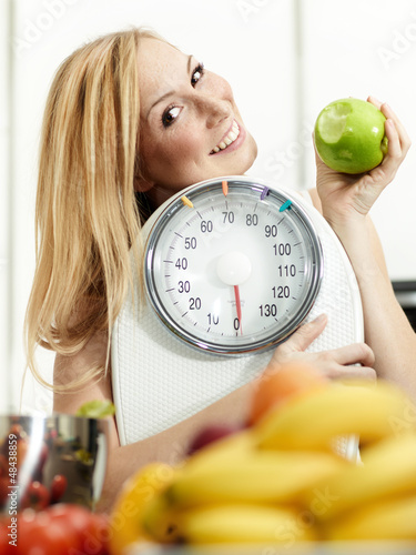 Photo: Girl with scale and fruits in the kitchen is proud to lose weigh Girl with scale and fruits in the kitchen is proud to lose weigh