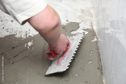 Photo: Construction worker is tiling at home tile floor adhesive Construction worker is tiling at home tile floor adhesive