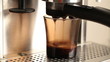Coffee pours in dark glass cup in espresso coffee machine