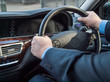 Chauffeur's hands on the steering wheel of a luxury car