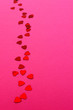 Trail of red heart shaped confetti on pink paper