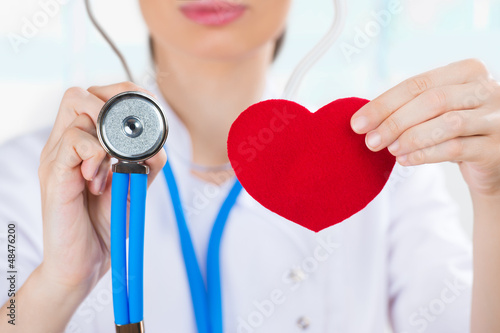 Photo: Female doctor with stethoscope holding red human heart at hospit Female doctor with stethoscope holding red human heart at hospit
