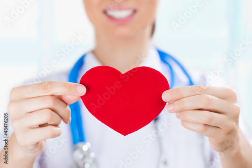 Photo: Female doctor with stethoscope holding red human heart at hospit Female doctor with stethoscope holding red human heart at hospit