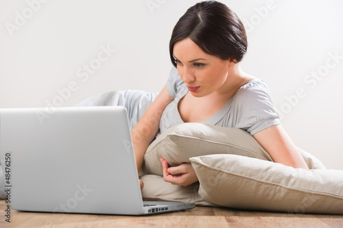 Photo: A young woman lying on the floor with laptop at home A young woman lying on the floor with laptop at home
