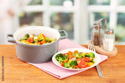 Photo: Vegetable stew in gray pot on wooden table on bright background Vegetable stew in gray pot on wooden table on bright background