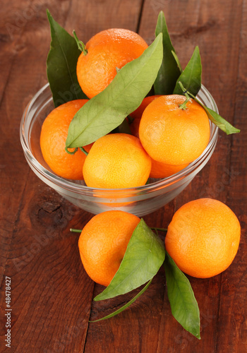 Photo: Sweet tangerines with leaves, on wooden background Sweet tangerines with leaves, on wooden background