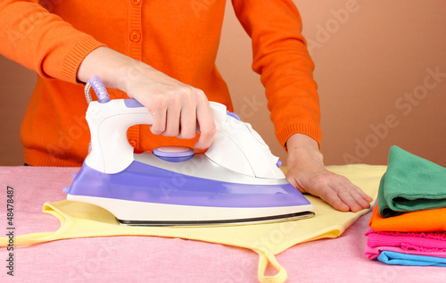 Photo: Young woman ironing her clothes, on brown background Young woman ironing her clothes, on brown background