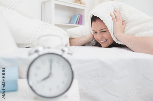 Photo: Woman covers ears with sheet as alarm clock rings Woman covers ears with sheet as alarm clock rings