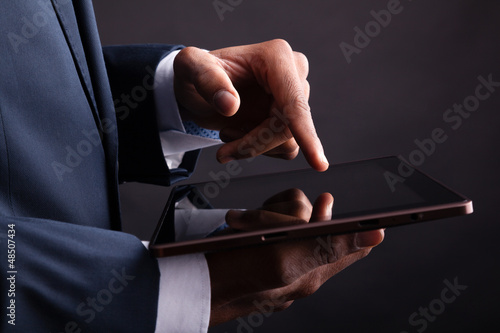 Photo: Closeup of businessman holding digital tablet on black backgroun Closeup of businessman holding digital tablet on black backgroun