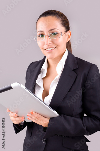 Photo: Young smiling business woman with tablet computer on grey backgr Young smiling business woman with tablet computer on grey backgr