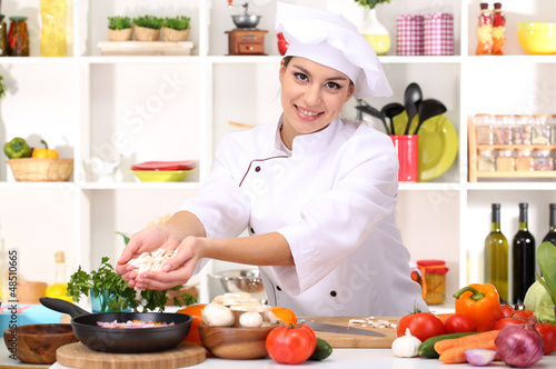 Photo: Young woman chef cooking in kitchen Young woman chef cooking in kitchen